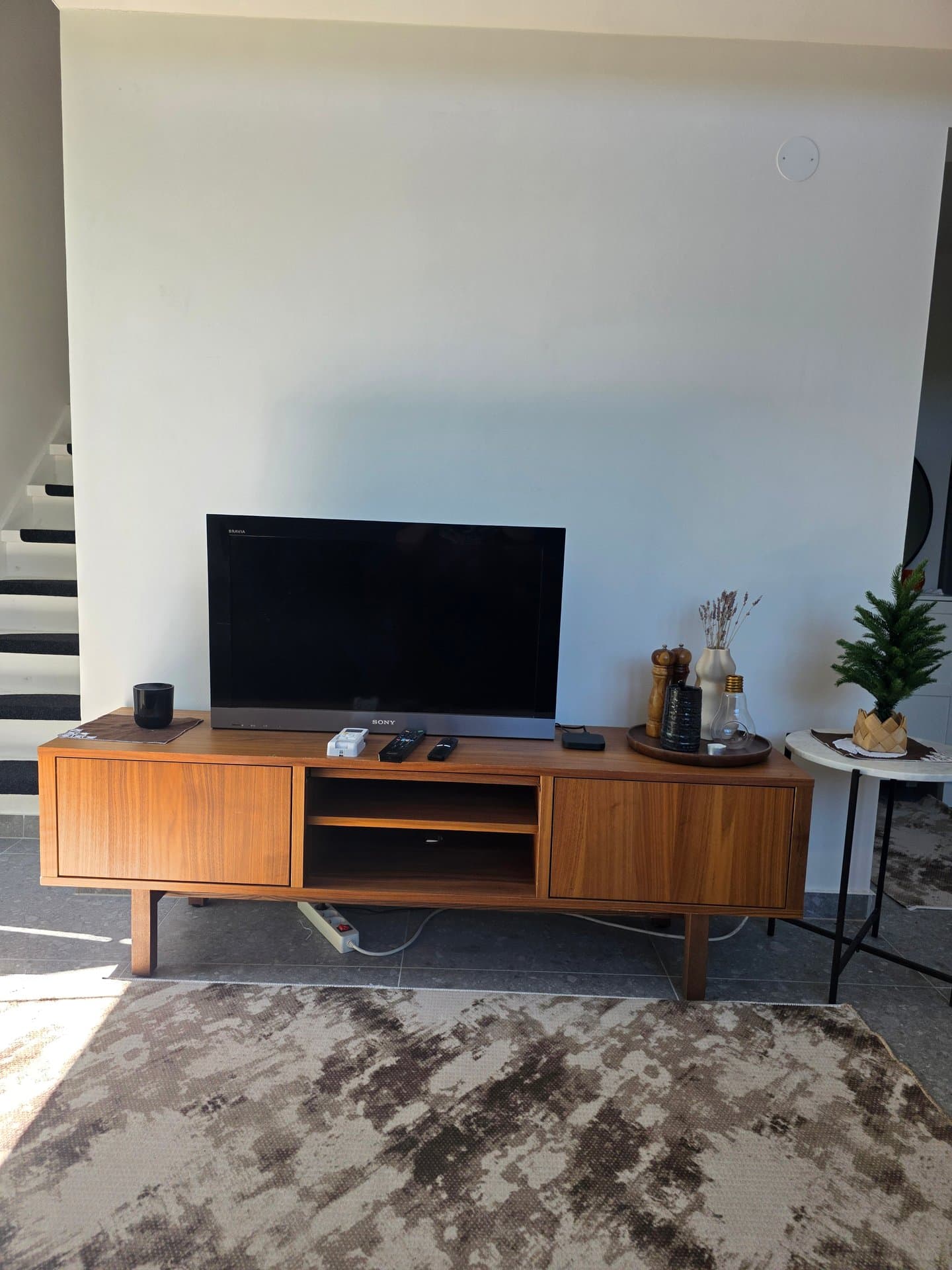 Modernt vardagsrum med stilfull Sony-TV monterad på vit vägg, vintage träverk-TV-bänk och skandinavisk inredning. Perfekt för avkoppling med naturligt ljus och minimalistisk design.